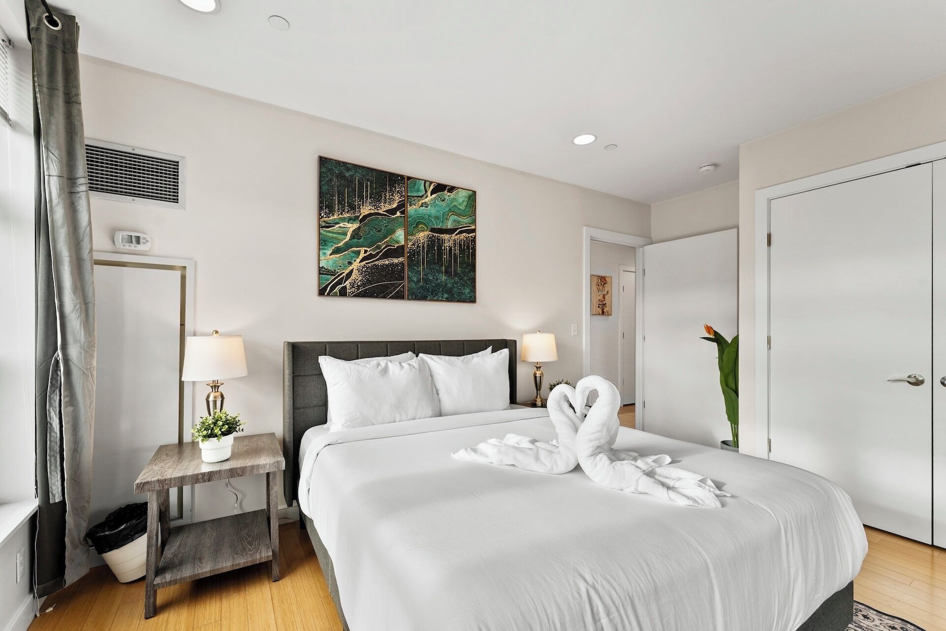 Une chambre d’hôtel avec un grand lit, deux tables de chevet avec des lampes, un climatiseur fixé au mur, une porte et une plante en pot.