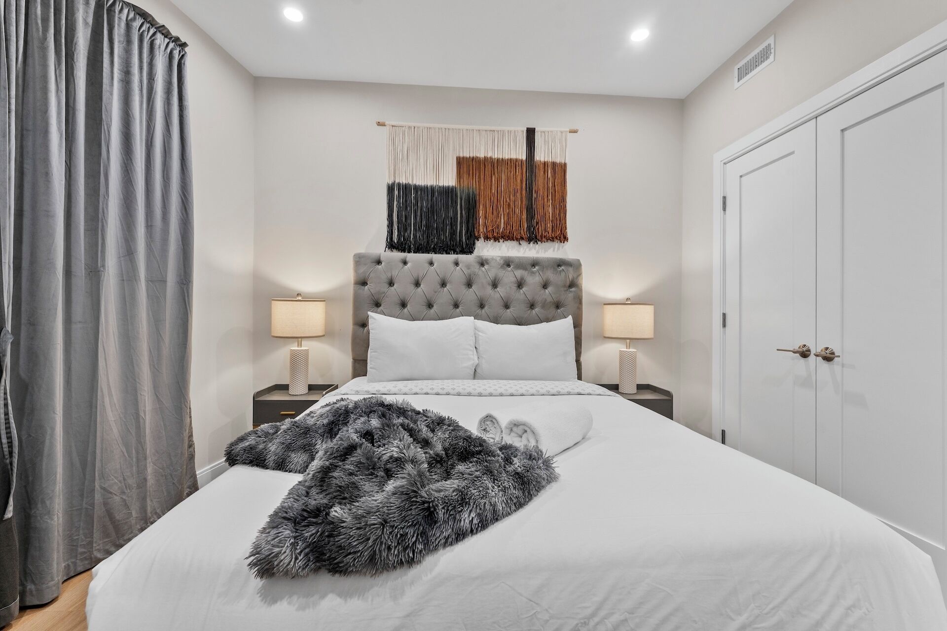 Une chambre à coucher avec une tête de lit capitonnée, deux lampes de chevet, un plaid moelleux et une grande armoire.