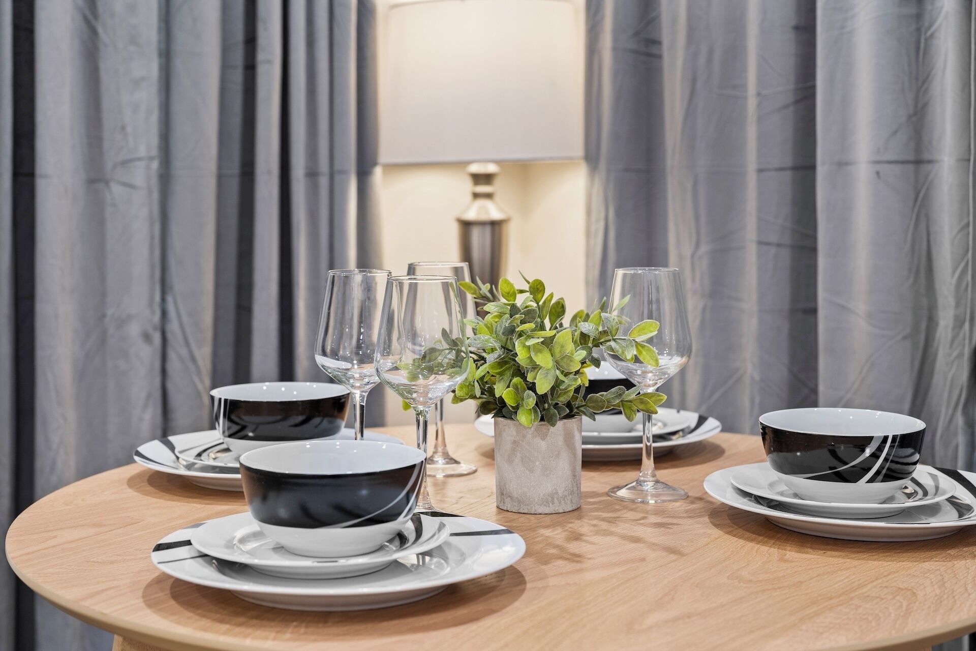 A round dining table with a central plant, surrounded by plates, bowls, and wine glasses.