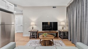 A modern living room with a flat-screen TV, two side tables with lamps, a wooden coffee table, and a sofa. - Luxury 2BR near Cambridge (Somerville)