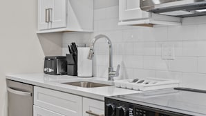 A modern kitchen with white cabinetry, a stainless steel sink, a built-in dishwasher, and a digital oven control panel. - Luxury 2BR near Cambridge (Somerville)