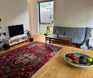 A living room with a flat-screen TV, a grey sofa, a wooden coffee table, and a red patterned rug. - Cozy 2BDR Ivanhoe Unit with Modern Amenities (Ivanhoe)