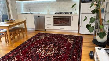 A modern kitchen with white cabinetry, a dishwasher, a stove, and a microwave. There is a dining table with chairs and a large patterned rug.