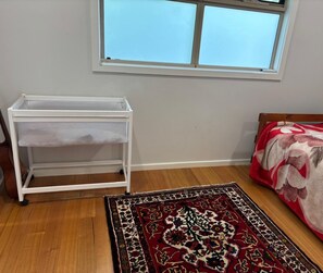 A room with a white storage unit, a patterned rug, a bed with a floral bedspread, and a window with a view.