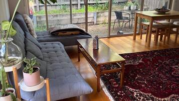 A cozy living room with a grey sofa, a coffee table, and a patterned rug. There are potted plants and a glass vase on a side table.