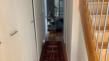 A hallway with a patterned rug, a staircase with wooden steps, and a door leading to a room with a bed and a plant.