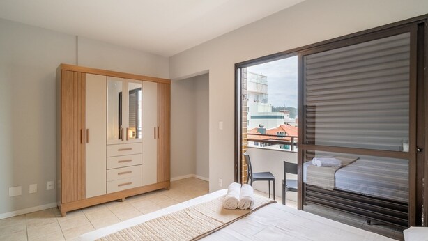 Une chambre avec une grande armoire, un lit sur lequel est posée une serviette enroulée, et une vue sur les immeubles à travers une porte coulissante.