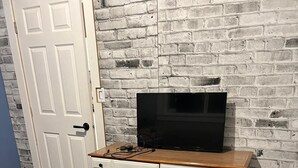 A room with a white dresser against a brick wall, a flat-screen TV on top, and a wooden floor. - Secondary private 1 bdrm / 1 bath suite in Fanny Bay (Comox Valley A)