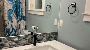 A bathroom with a white sink, a black faucet, a blue shower curtain with a sea creature design, and a window above the sink. - Secondary private 1 bdrm / 1 bath suite in Fanny Bay (Comox Valley A)