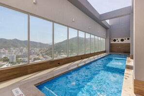 A swimming pool with a city view, wooden floor, and a wooden wall with circular cutouts. - U-GO Edificio Ambar Roca en Rodadero Sur (Santa Marta)