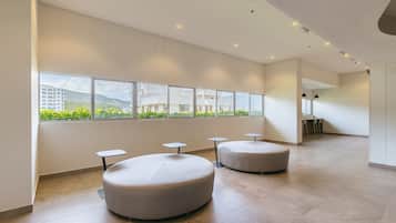 Un hall d’entrée spacieux, doté de grandes fenêtres, d’espaces de détente aménagés avec des sièges circulaires, et d’une salle à manger visible au fond.