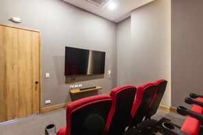 A room with a flat-screen TV mounted on the wall, a wooden door, and red and black upholstered chairs. - U-GO Edificio Ambar Roca en Rodadero Sur (Santa Marta)