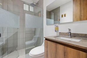 A bathroom with a glass shower enclosure, a toilet, a sink with a wooden vanity, and a mirror. - U-GO Edificio Ambar Roca en Rodadero Sur (Santa Marta)