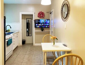 A kitchen with a stove, sink, and a TV mounted on the wall displaying a movie.