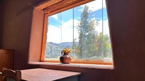 A room with a wooden table and chair, a window with a view of mountains, and a vase with flowers on the windowsill. - 1BR Country Home w/ Garden & Mountain View (Taray)