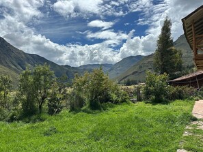 A rural landscape with a wooden cabin, lush green fields, and mountains in the background. - 1BR Country Home w/ Garden & Mountain View (Taray)