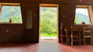 A rustic room with wooden beams, a wooden table with chairs, and a view of green hills through open doors. - 1BR Country Home w/ Garden & Mountain View (Taray)
