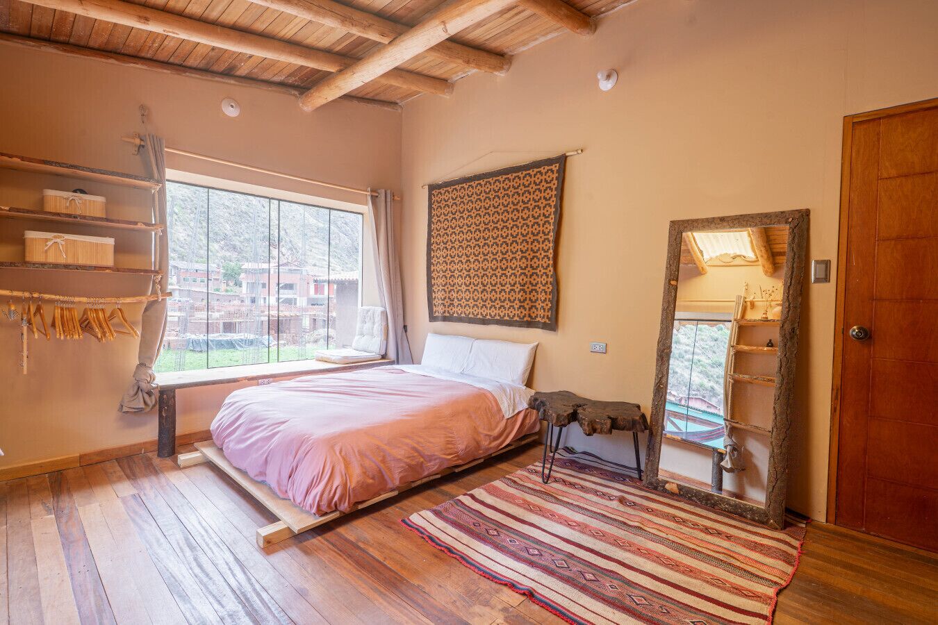 Une chambre à coucher avec un lit, une fenêtre, une échelle en bois, un tapis à motifs et une porte.