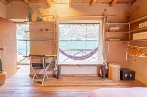 Ein Zimmer mit einer Hängematte, Holzböden, einem Schreibtisch und Blick auf ein Gewässer.