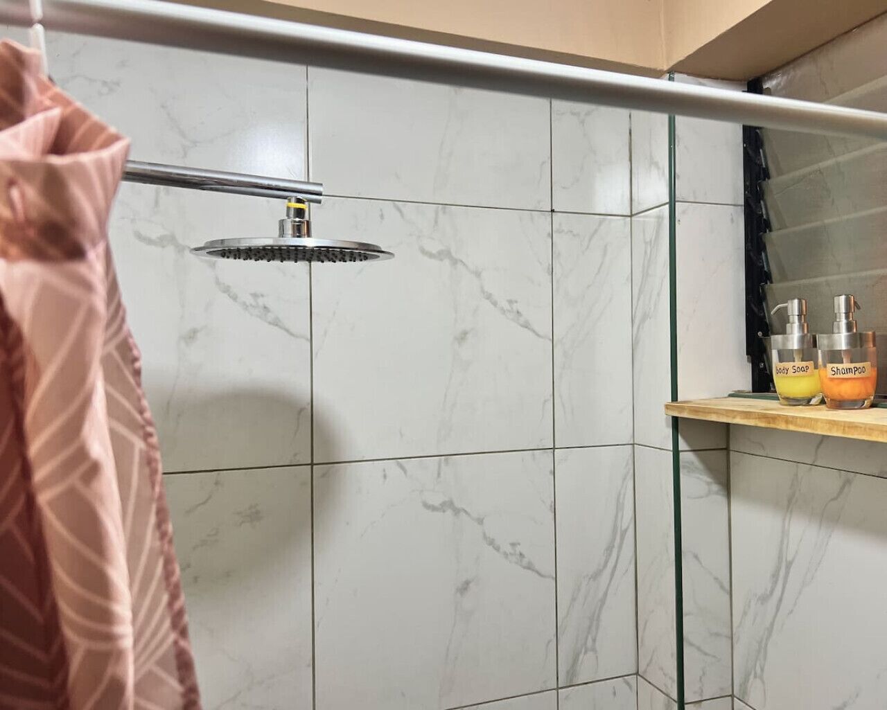 A bathroom with a shower, marble tiles, and a shelf with toiletries.