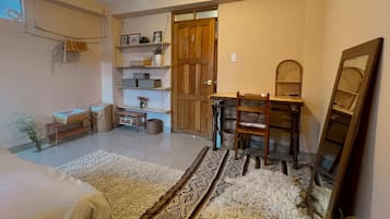 A cozy room with a bed, a desk, and a chair. There are shelves with items and a door leading to another room.