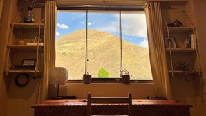 Una habitación con un ventanal grande, un escritorio de madera y estanterías con diversos objetos.
