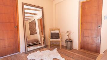 A room with wooden flooring, a white fur rug, a wooden chair, a small table with a vase, and two wooden doors.