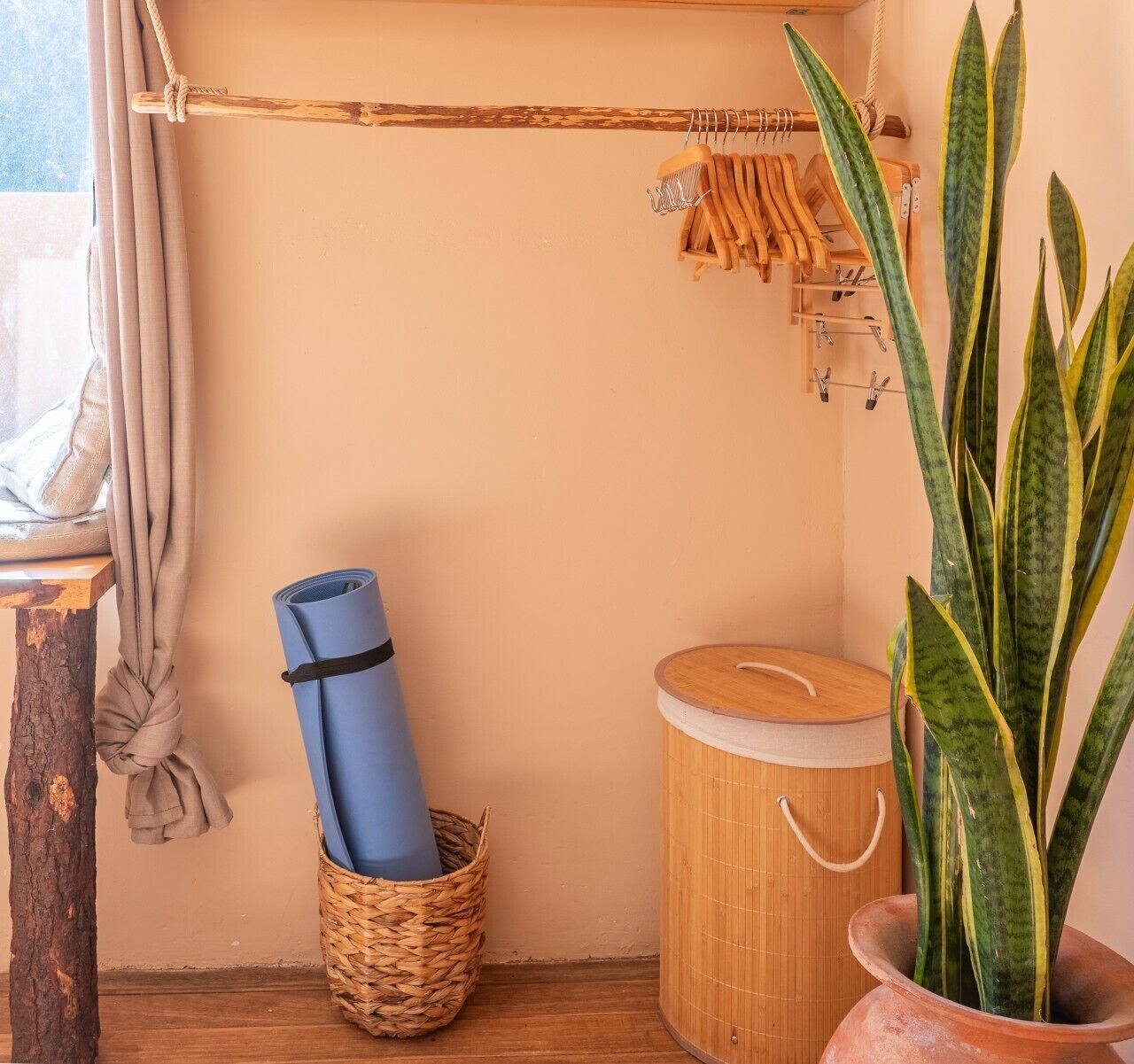 Un coin de pièce avec un plancher en bois, un panier en osier contenant un tapis enroulé, un récipient en bambou et une plante en pot.