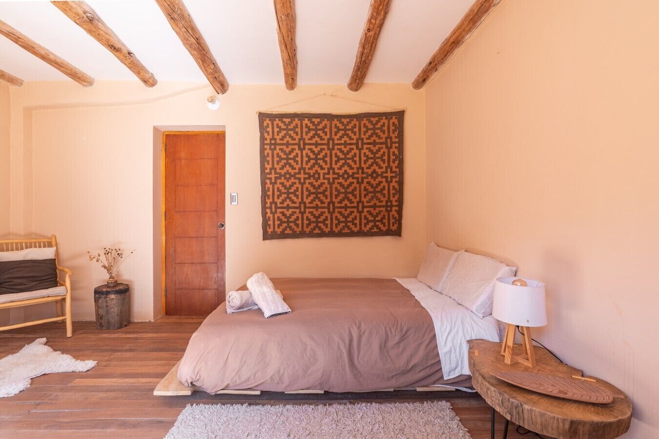 Une chambre à coucher avec un lit, un banc en bois, une porte et une tapisserie à motifs.
