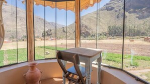 A room with a view of a mountainous landscape, a rustic wooden chair, and a terracotta pot.