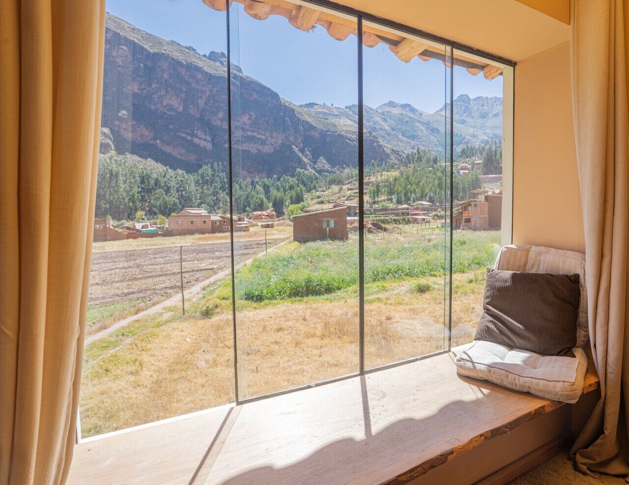 Una habitación con un amplio ventanal que ofrece vistas a un paisaje montañoso y un pueblo lejano.