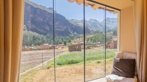 A room with a large window offering a view of a mountainous landscape and a distant village.