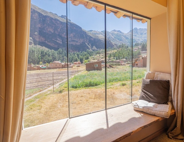 Una habitación con un amplio ventanal que ofrece vistas a un paisaje montañoso y un pueblo lejano.