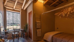 A cozy bedroom with a wooden bed, a wooden table with chairs, a ladder with towels, and a large window with a view of the outdoors.
