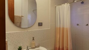 A bathroom with a round mirror, a sink with a plant, a shower curtain, and tiled walls.