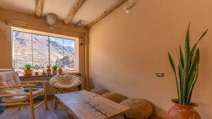 A cozy room with a wooden table, two chairs, a large window with a mountain view, and a potted plant.