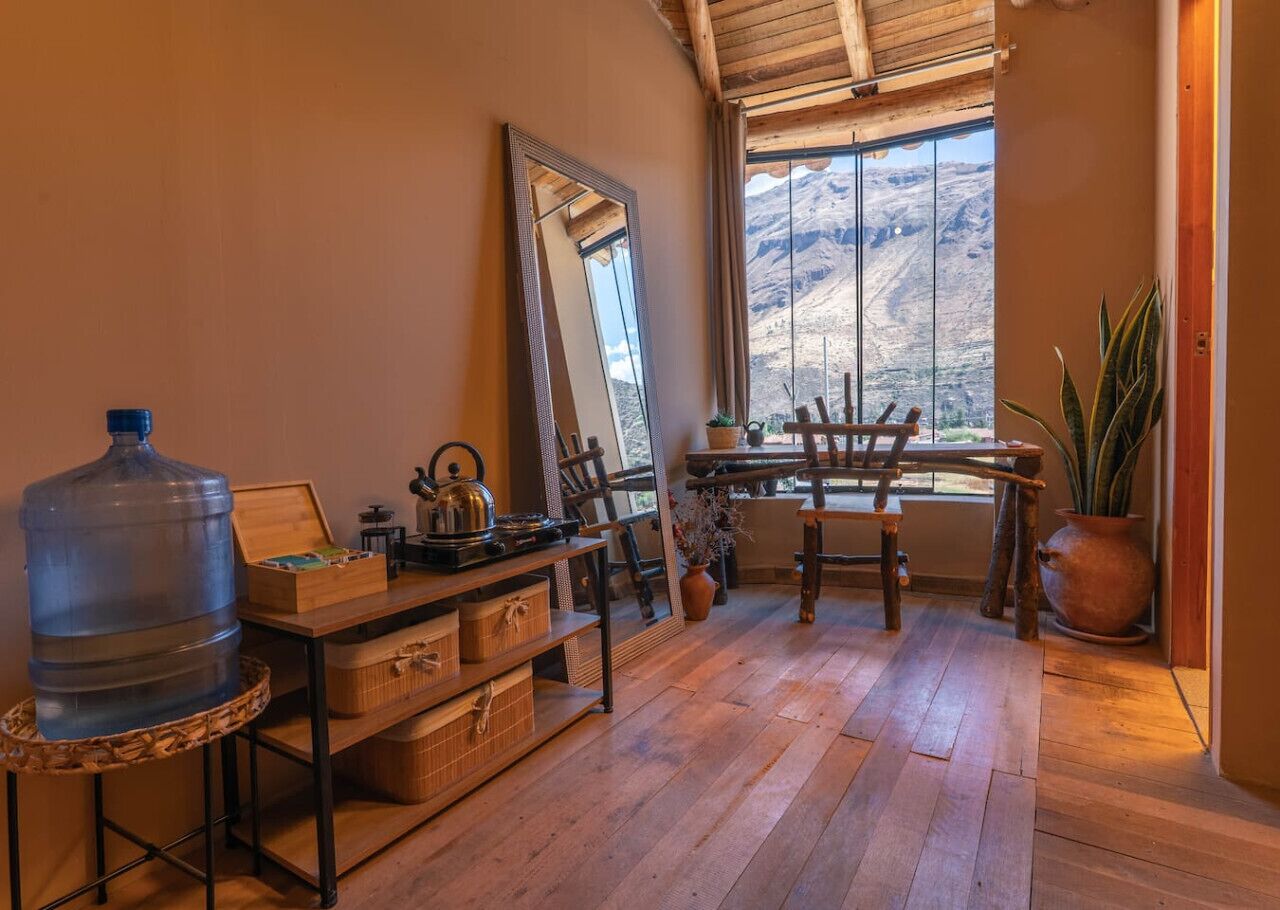 Une pièce rustique avec un plancher en bois, un grand distributeur d’eau, un miroir, une table avec des chaises et une vue sur les montagnes par la fenêtre.