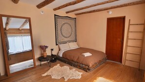 Une chambre avec un plafond en bois, un grand lit, une échelle en bois, un miroir et une tapisserie à motifs.