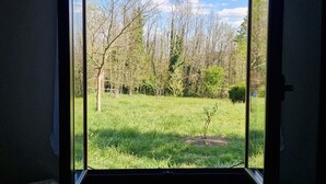 A room with a large window, a radiator, and a white sofa. - Single-storey apartment on large wooded garden with swimming pool (Sarlat-la-Canéda)