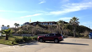 A red SUV parked in a parking lot with a building in the background. - BSI 106--Studio with Ocean View, Sleeps 2 Adults/2 Kids, Pool, Dogs OK! (Port Aransas)