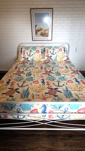 Una cama con una colcha de motivos marinos coloridos, una pared de ladrillo blanco y un cuadro colgado sobre la cama.