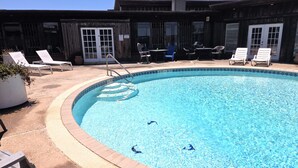 A swimming pool with lounge chairs and a wooden building in the background. - BSI 106--Studio with Ocean View, Sleeps 2 Adults/2 Kids, Pool, Dogs OK! (Port Aransas)