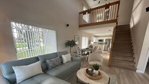 Ein modernes Wohnzimmer mit einem grauen Ecksofa, einem runden Couchtisch und einer Treppe, die zu einer oberen Ebene führt.