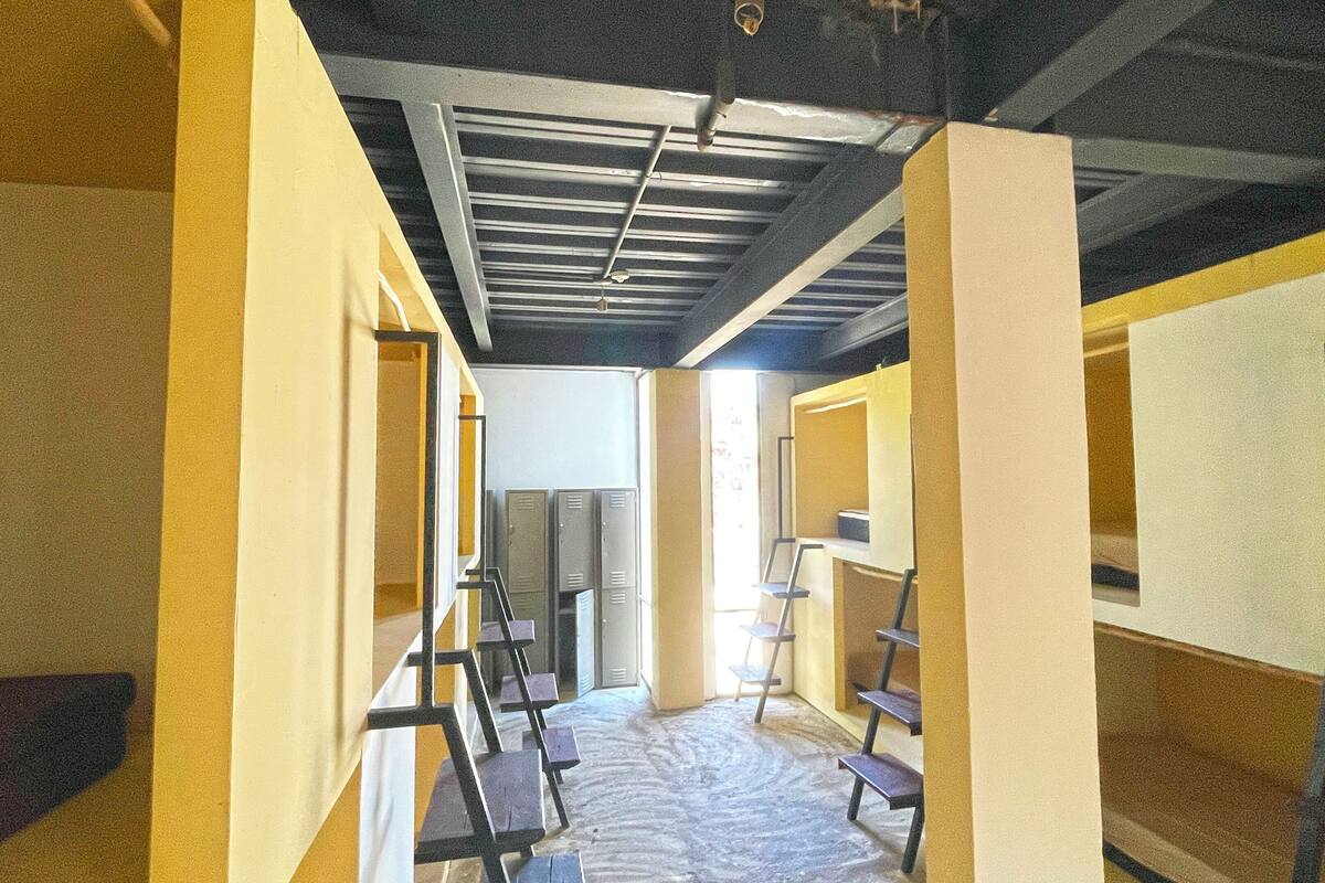 A corridor with bunk beds, lockers, and a ceiling with exposed beams.