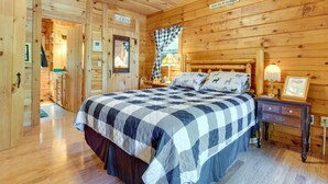 Ett sovrum inrett i stugstil med en stor säng, en sänggavel i trä, ett nattduksbord med en lampa och en skylt med texten ”The Cabin”.