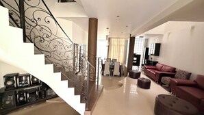Amplia sala de estar con una escalera que presenta barandales metálicos ornamentados, un sofá de cuero y un televisor instalado en la pared.