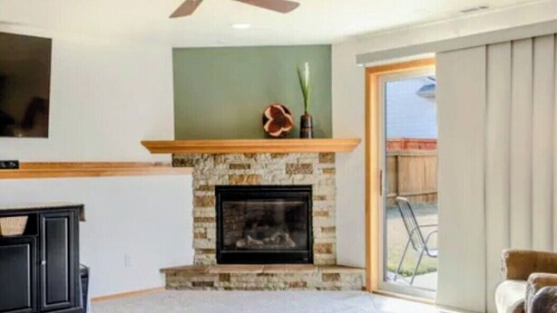 A living room with a stone fireplace, a television mounted on the wall, and a sliding glass door leading to an outdoor area. - Charming 2-bedroom bed & breakfast in serene Sioux Falls (Sioux Falls)