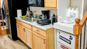 A kitchen with wooden cabinets, a black refrigerator, a microwave, a coffee maker, and a sink. - Charming 2-bedroom bed & breakfast in serene Sioux Falls (Sioux Falls)