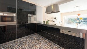 A modern kitchen with a stone backsplash, stainless steel appliances, and a view of a coastal landscape.