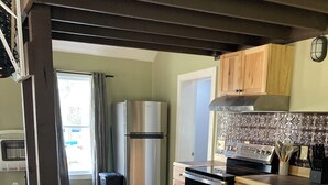 Een moderne keuken met roestvrijstalen apparatuur, houten kastjes en een grijze bank in een woonruimte.